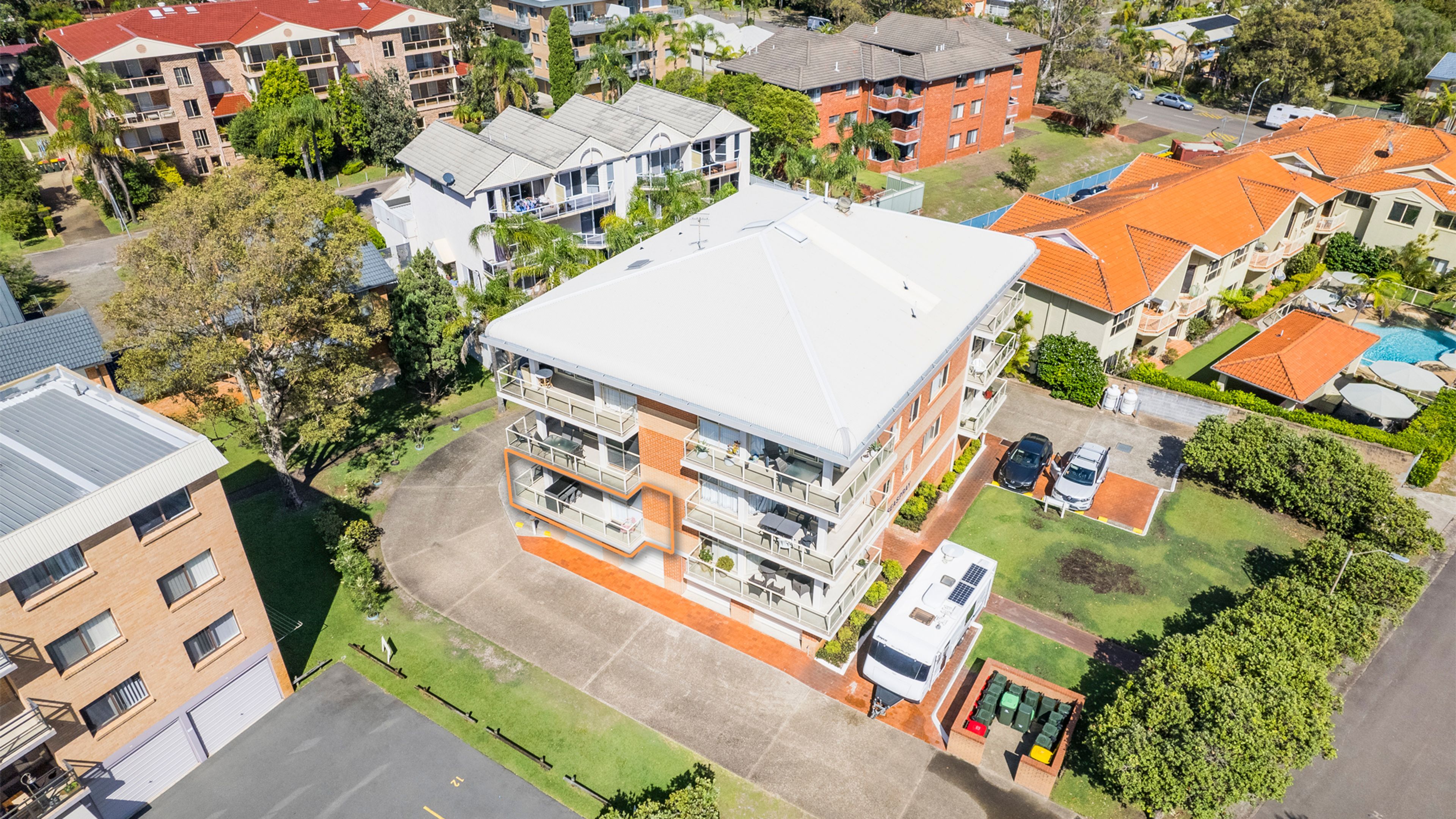 A multi-story residential building with balconies, a swimming pool, and a parking area.