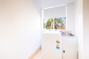 A compact laundry room with a washing machine, a sink, and a window. - Seaspray Sands Coastal Retreat in Nelson Bay (Nelson Bay)