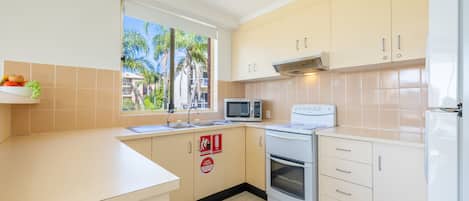 A kitchen with a microwave, oven, and a window with a view of palm trees.