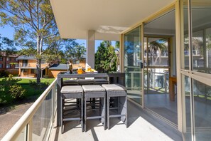 A balcony with wicker furniture and a glass door leading to an outdoor area. - Seaspray Sands Coastal Retreat in Nelson Bay (Nelson Bay)