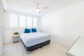 A bedroom with a bed, a ceiling fan, a window with blinds, a small table with a plant, and a bedside table. - Seaspray Sands Coastal Retreat in Nelson Bay (Nelson Bay)