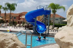 Une piscine avec un toboggan bleu, des chaises longues et des palmiers.