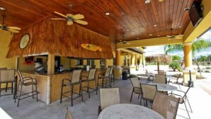 An outdoor seating area with wooden tables and chairs, a bar area with a thatched roof, and ceiling fans.