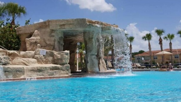 A pool with a waterfall feature, surrounded by rocks and palm trees.