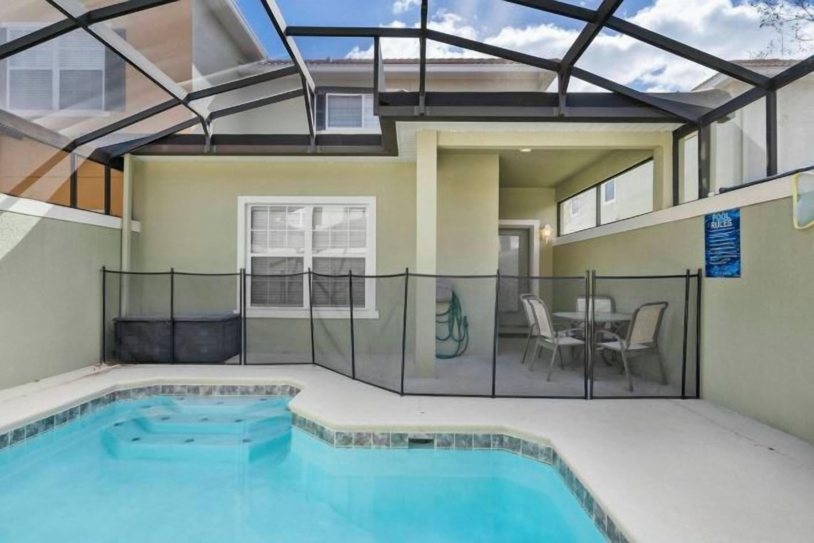A swimming pool with a glass enclosure, a covered patio area, and a view of the sky.