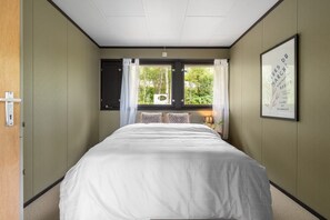 Ein Hotelzimmer mit einem großen Bett, einem Vorhangfenster, einem gerahmten Bild an der Wand und einer Tür mit Griff.