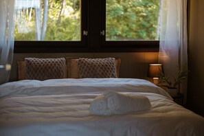 Ein ordentlich bezogenes Bett mit einem aufgerollten Handtuch, zwei strukturierten Kissen und einer Nachttischlampe.