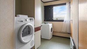 A compact laundry room with a front-loading washer and dryer, a window with curtains, and a view of the outside. - Top Floor Apartment with Scenic Views (Tromsø)