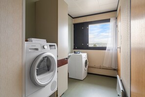 Ein kompakter Waschraum mit einer Frontlader-Waschmaschine und -Trockner, einem Fenster mit Vorhängen sowie Blick ins Freie.
