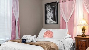 Een net opgemaakt bed met een wit-bruin dekbed, een roze kussen en een ingelijst foto aan de muur.