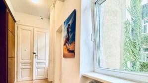 A hallway with wooden flooring, white walls, a radiator, and a window with a view of greenery outside. - Comfortable 5BR Stay Near Westbahnhof (Vienna)