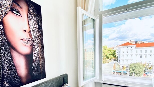 A bedroom with a bed, striped pillows, a large window, and a view of buildings outside. - Comfortable 5BR Stay Near Westbahnhof (Vienna)