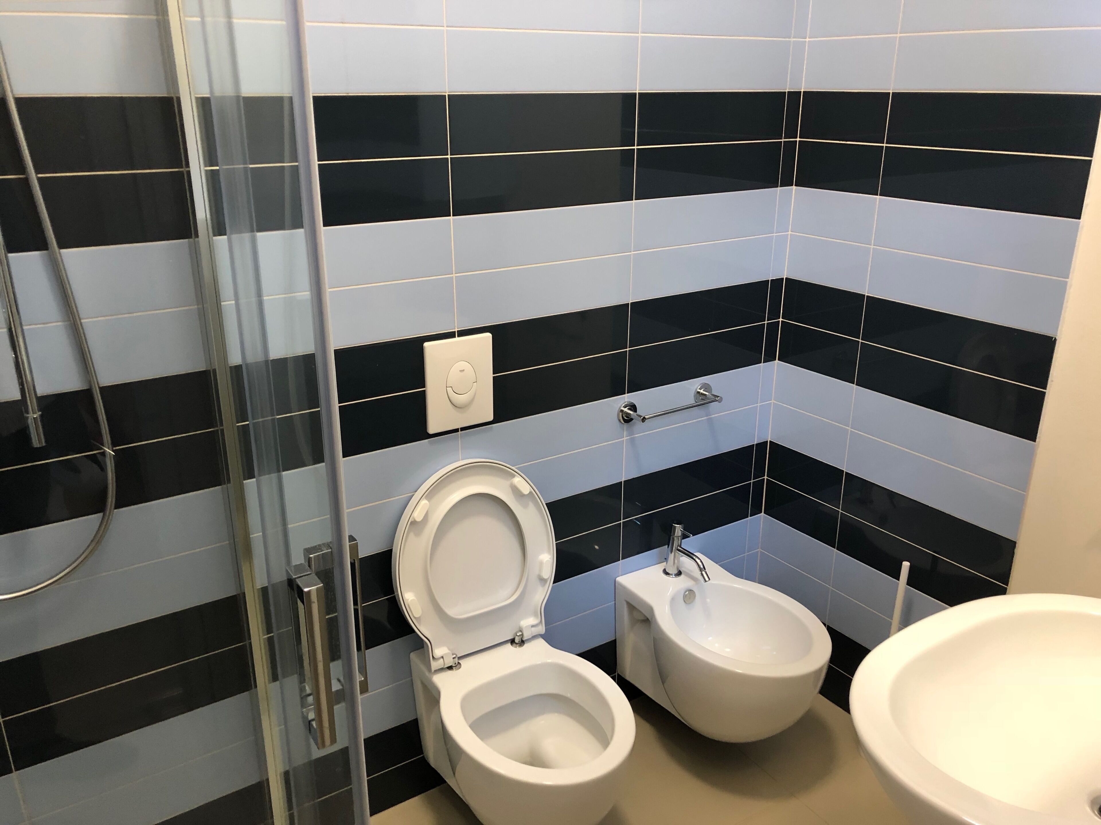 Een badkamer met toilet, bidet en wastafel, alles in het wit, met zwart-wit gestreepte tegels op de muren.