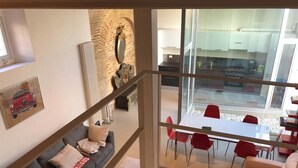 Ein modernes Wohnzimmer mit einem grauen Sofa, roten Sesseln und einem Essbereich mit einem Glastisch.