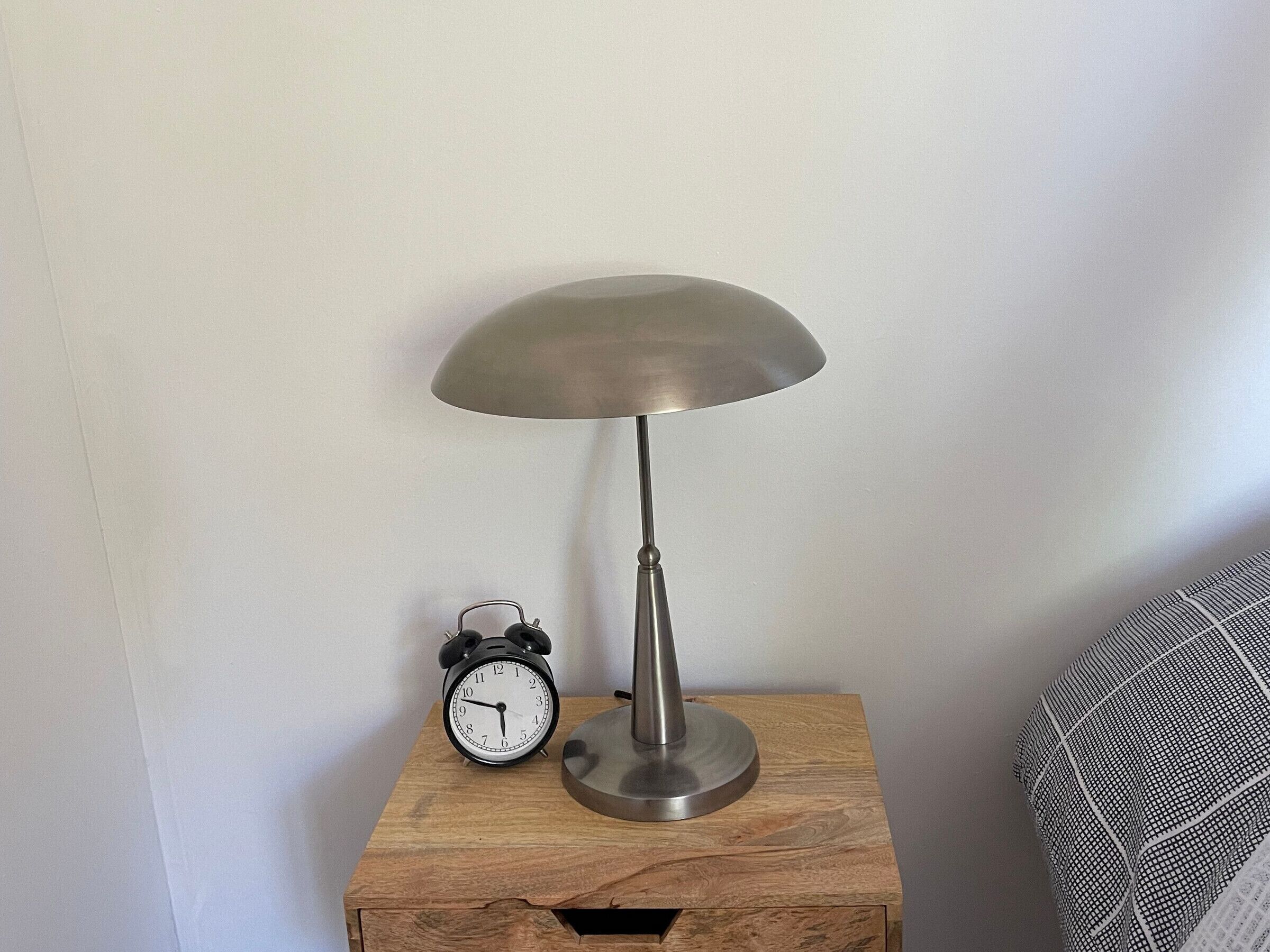 Une table de chevet en bois, agrémentée d’une lampe de table en métal et d’un réveil classique.