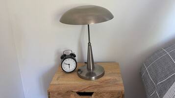 Une table de chevet en bois, agrémentée d’une lampe de table en métal et d’un réveil classique.