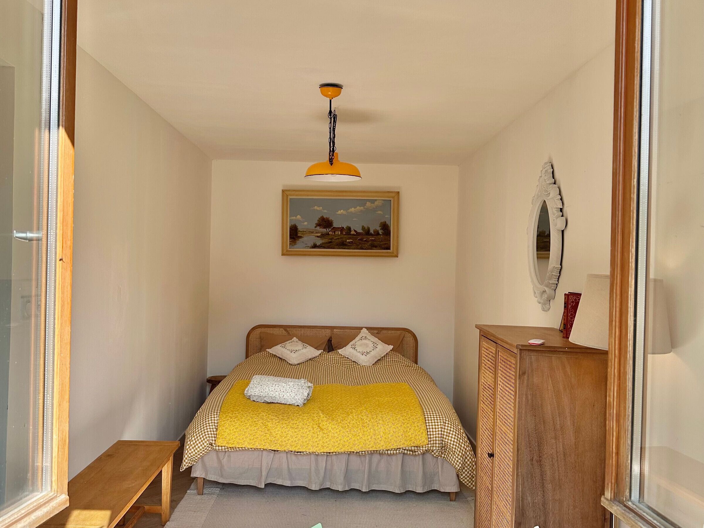 Une chambre à coucher avec un lit, un banc en bois, un miroir et un tableau accroché au mur.