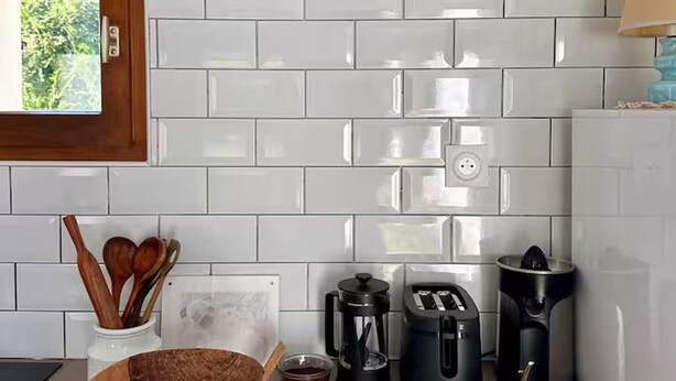 Une cuisine avec des carreaux de céramique blancs disposés en motif métro, une fenêtre, une machine à café, un grille-pain, un mixeur et des ustensiles en bois.