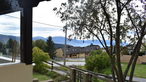 A view from a window overlooking a building with a sloped roof, surrounded by greenery and mountains in the background. - Comfortable 2-room apartment - 4 people - Garden in Font-Romeu (Font-Romeu-Odeillo-Via)