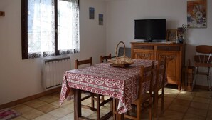 A dining area with a table set for four, a television on a wooden cabinet, and a window with lace curtains. - Comfortable 2-room apartment - 4 people - Garden in Font-Romeu (Font-Romeu-Odeillo-Via)