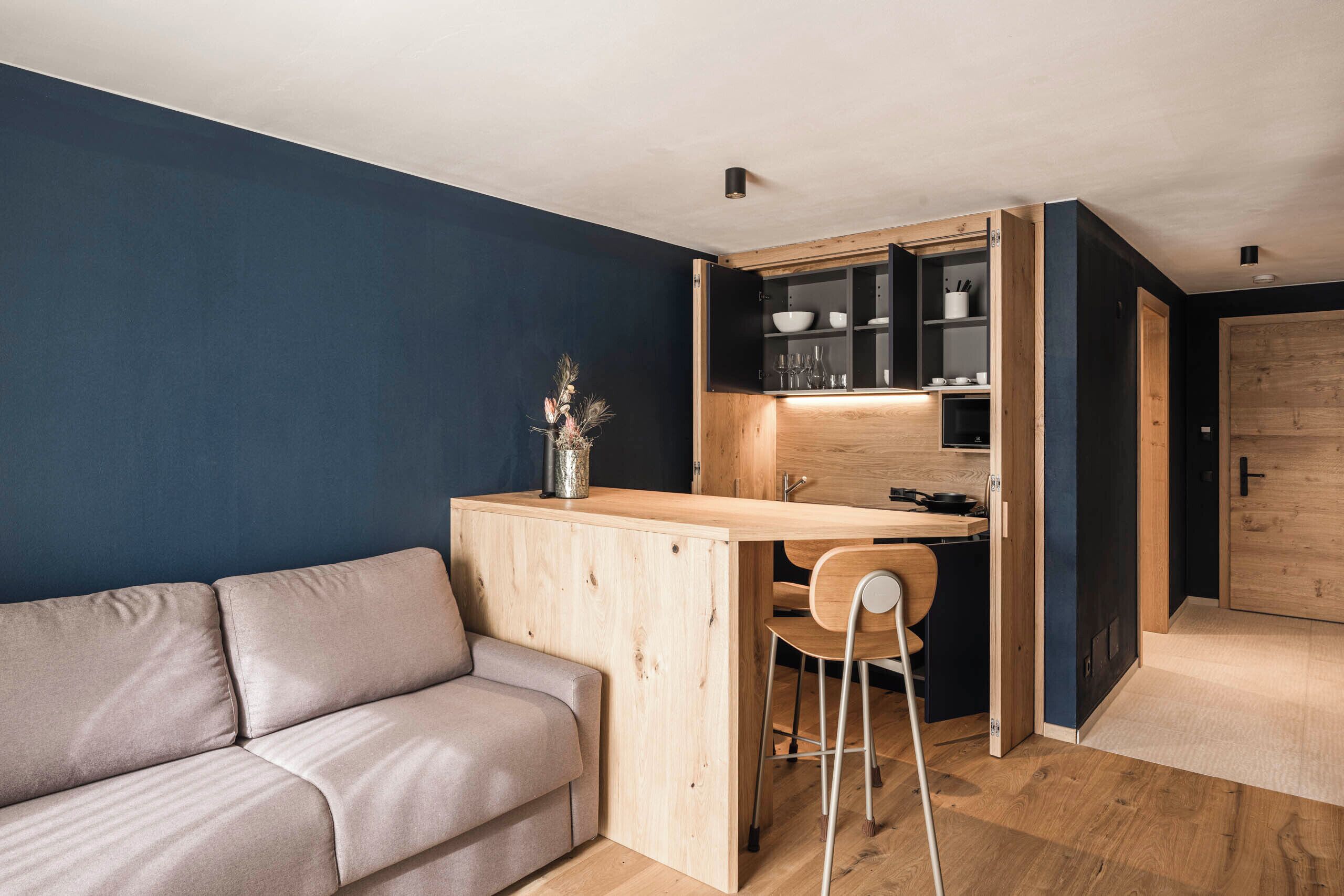 A compact living space with a wooden desk, a sofa, and a cabinet with shelves.