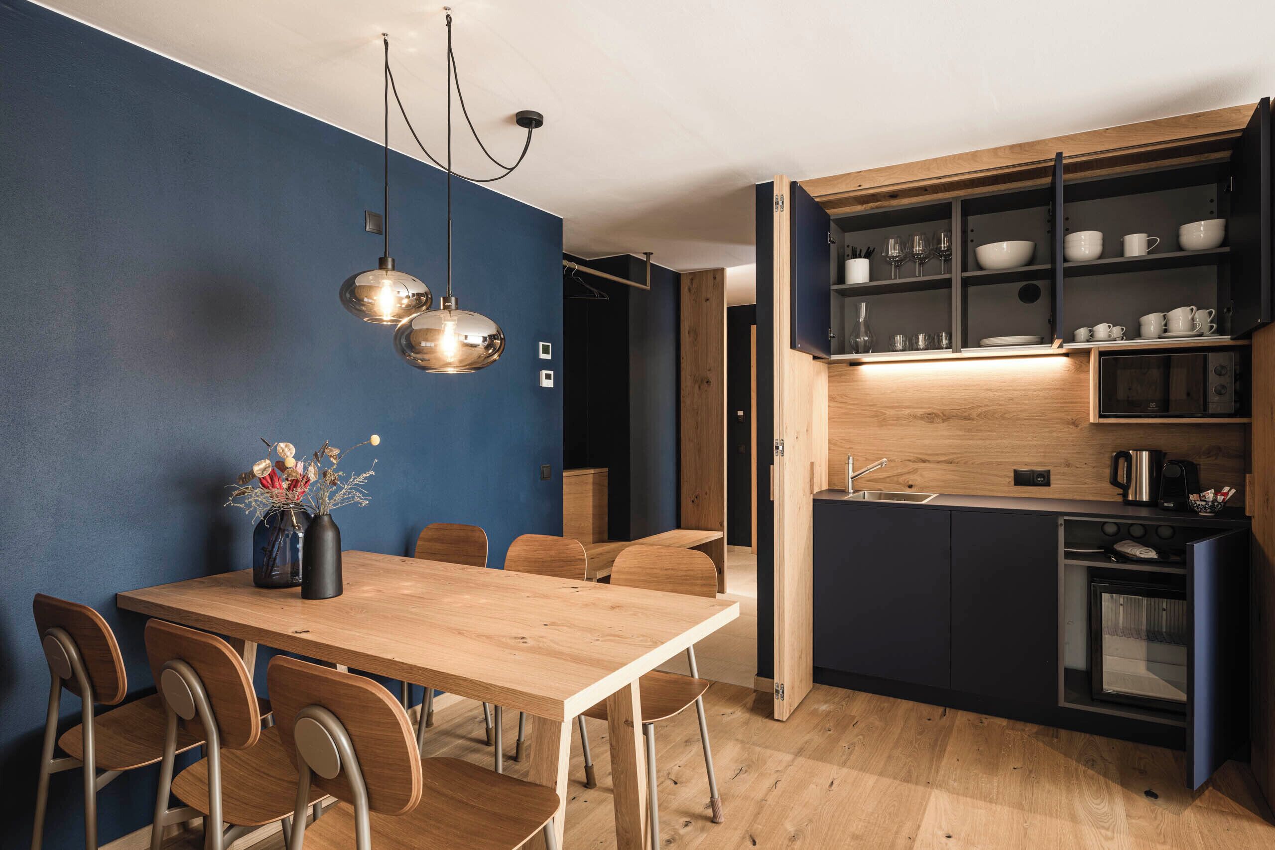 Una cocina moderna con armarios de madera, horno empotrado y una zona de comedor con mesa y sillas de madera.