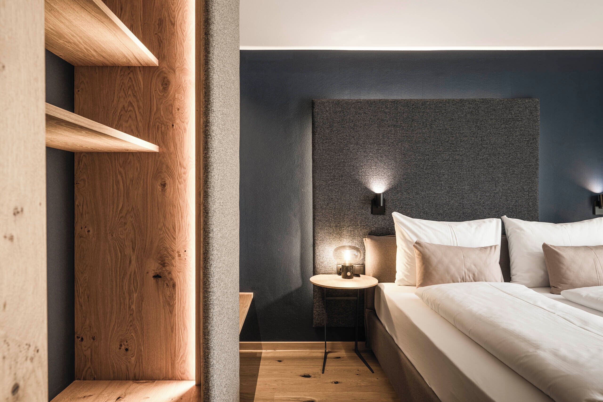 A modern bedroom with a wooden accent wall, a bedside table with a lamp, and a neatly made bed.