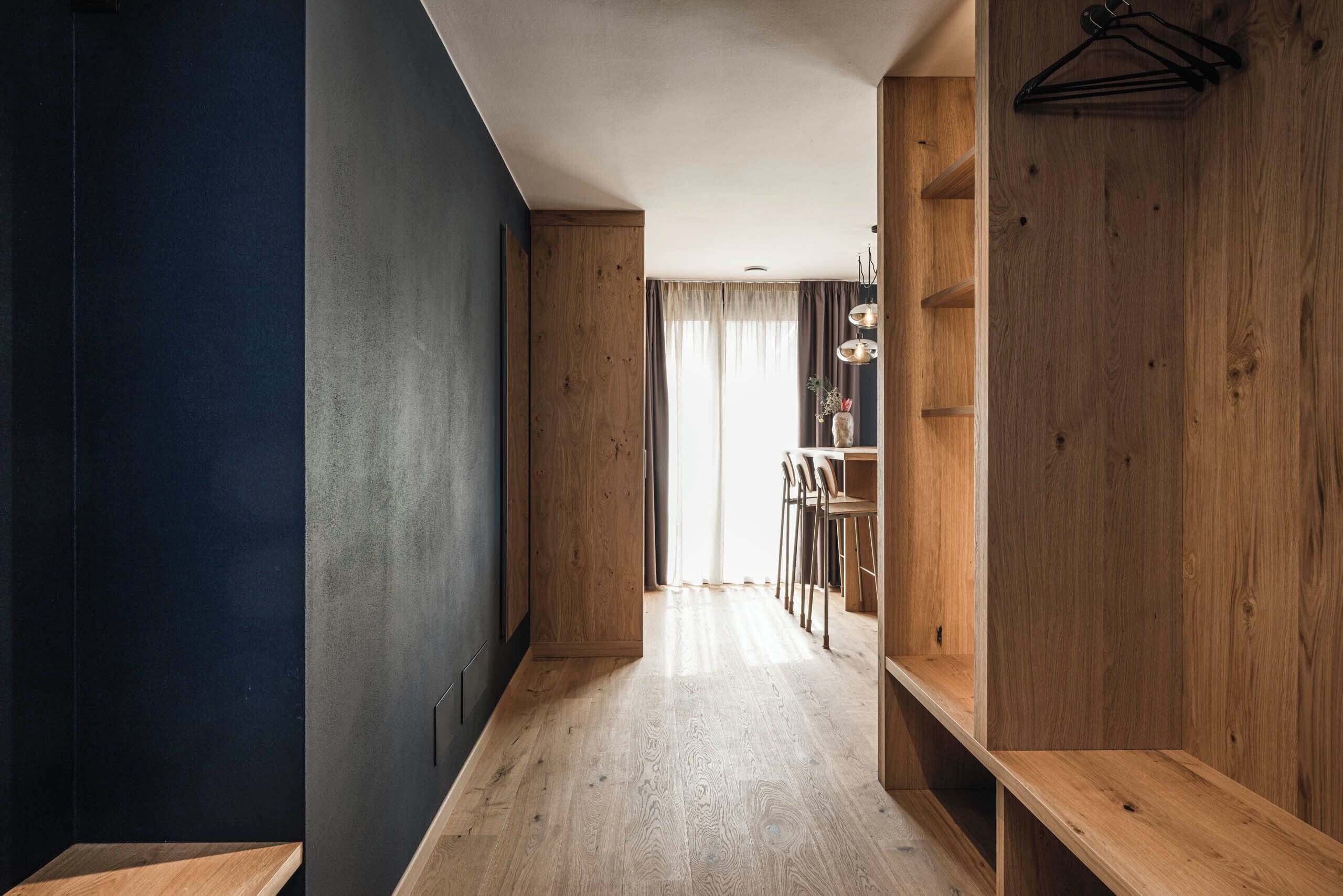 A hallway with wooden walls and a light-colored floor, leading to a dining area with chairs and a table.
