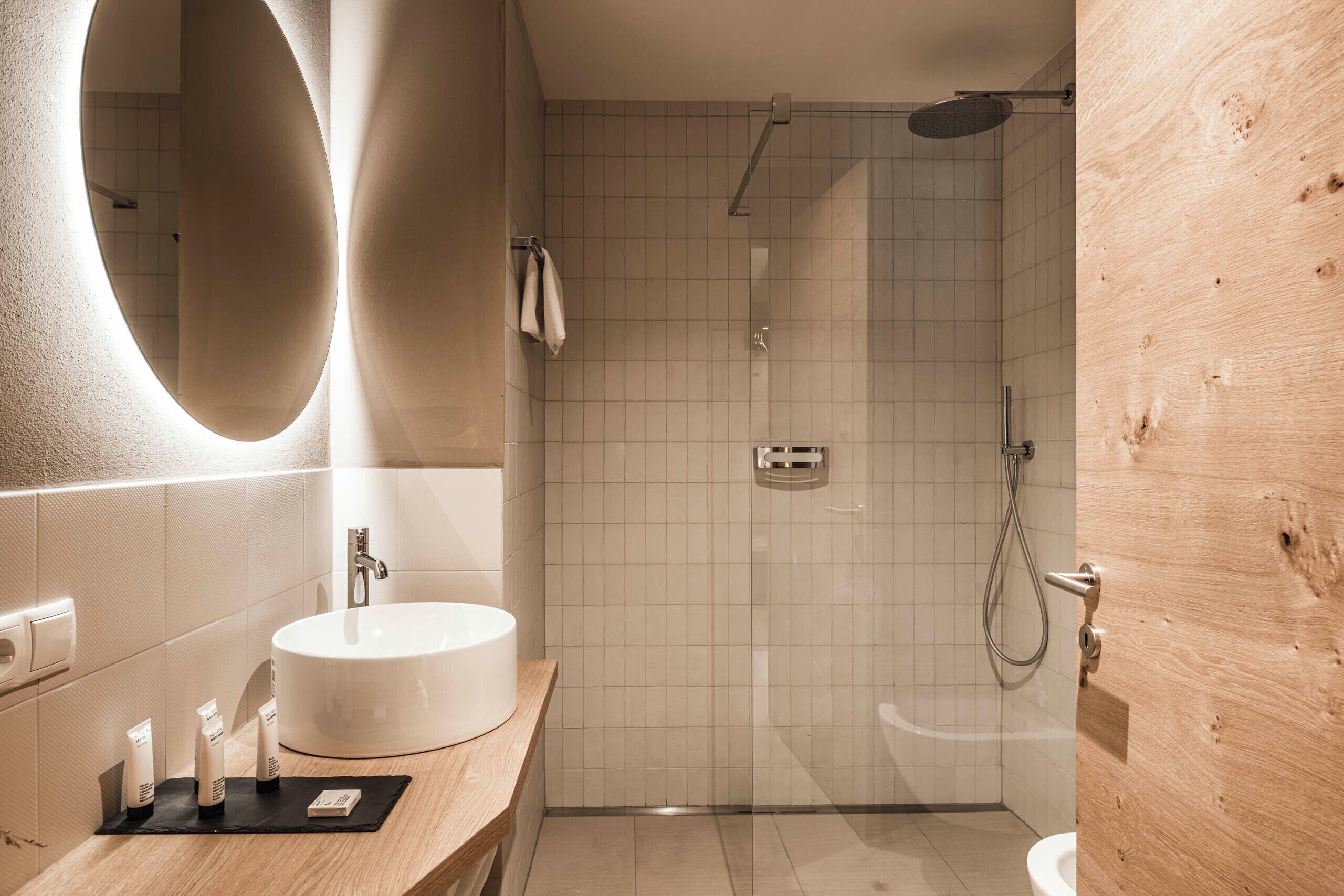 A modern bathroom with a round mirror, a sink, and a shower.