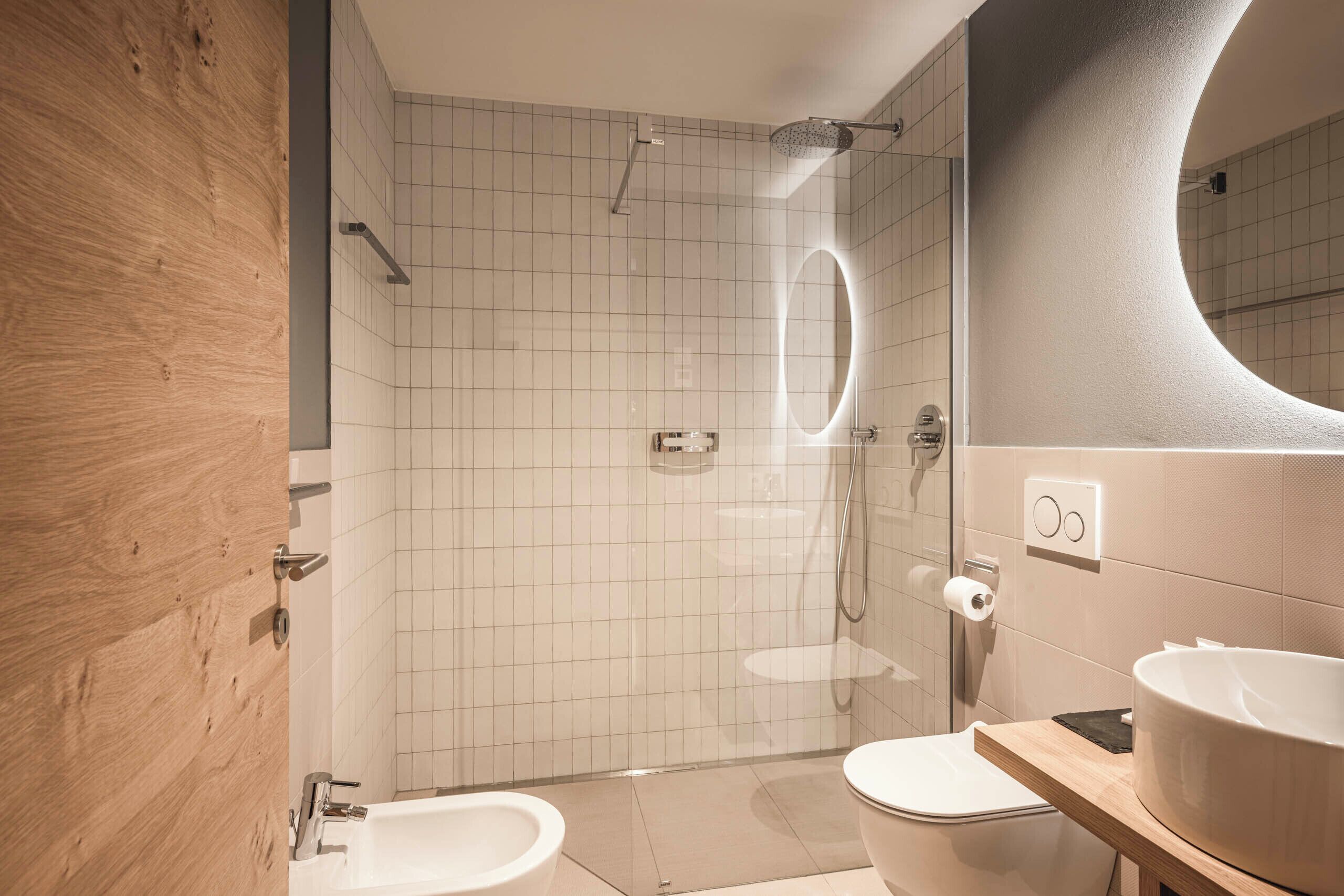 Un baño moderno con tocador de madera, bañera independiente, ducha con cerramiento de vidrio y un espejo grande.