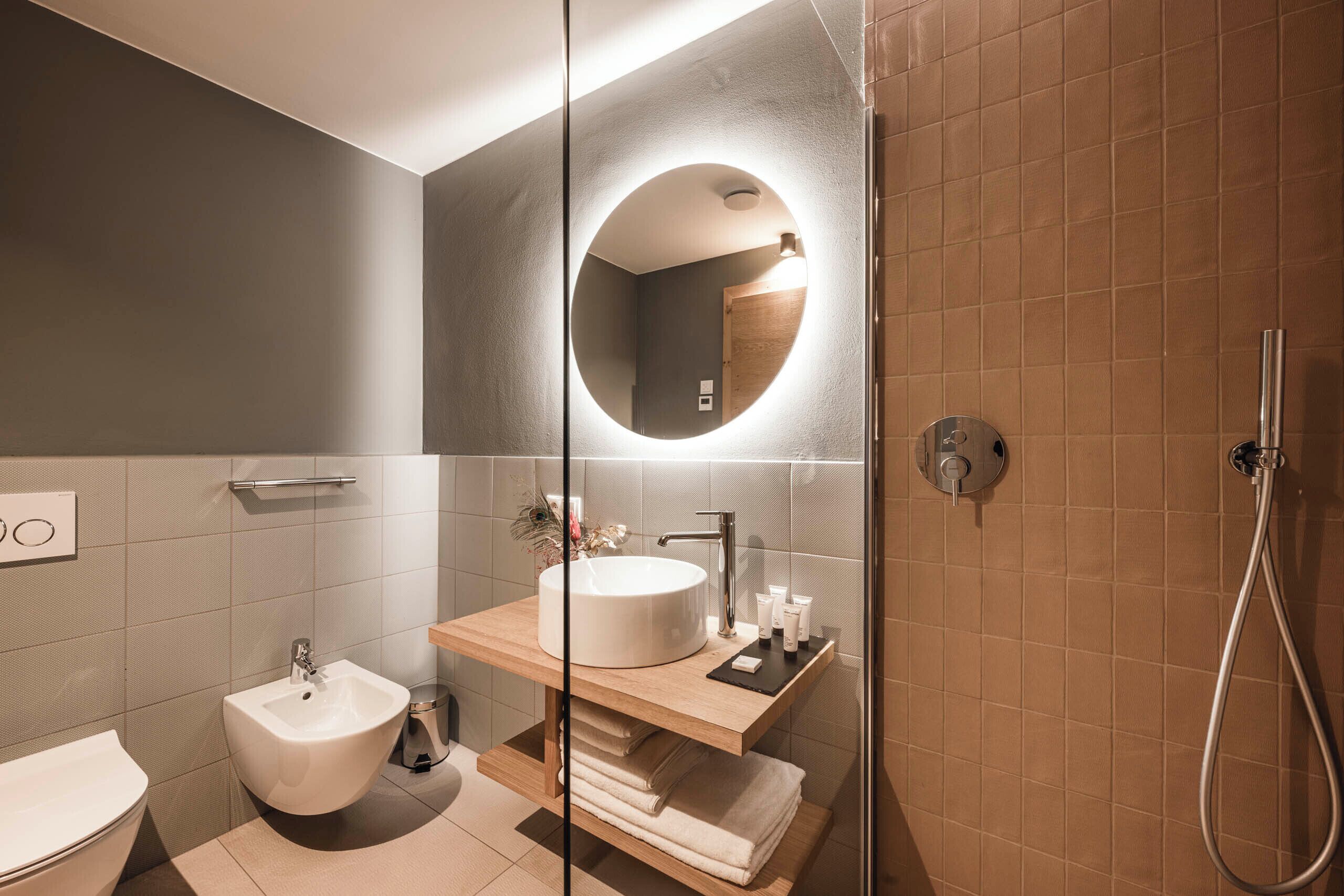 Un baño moderno con un espejo redondo, un lavamanos, un bidé y una ducha.