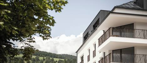 Un immeuble à plusieurs étages, doté de balcons et offrant une vue sur une colline boisée.