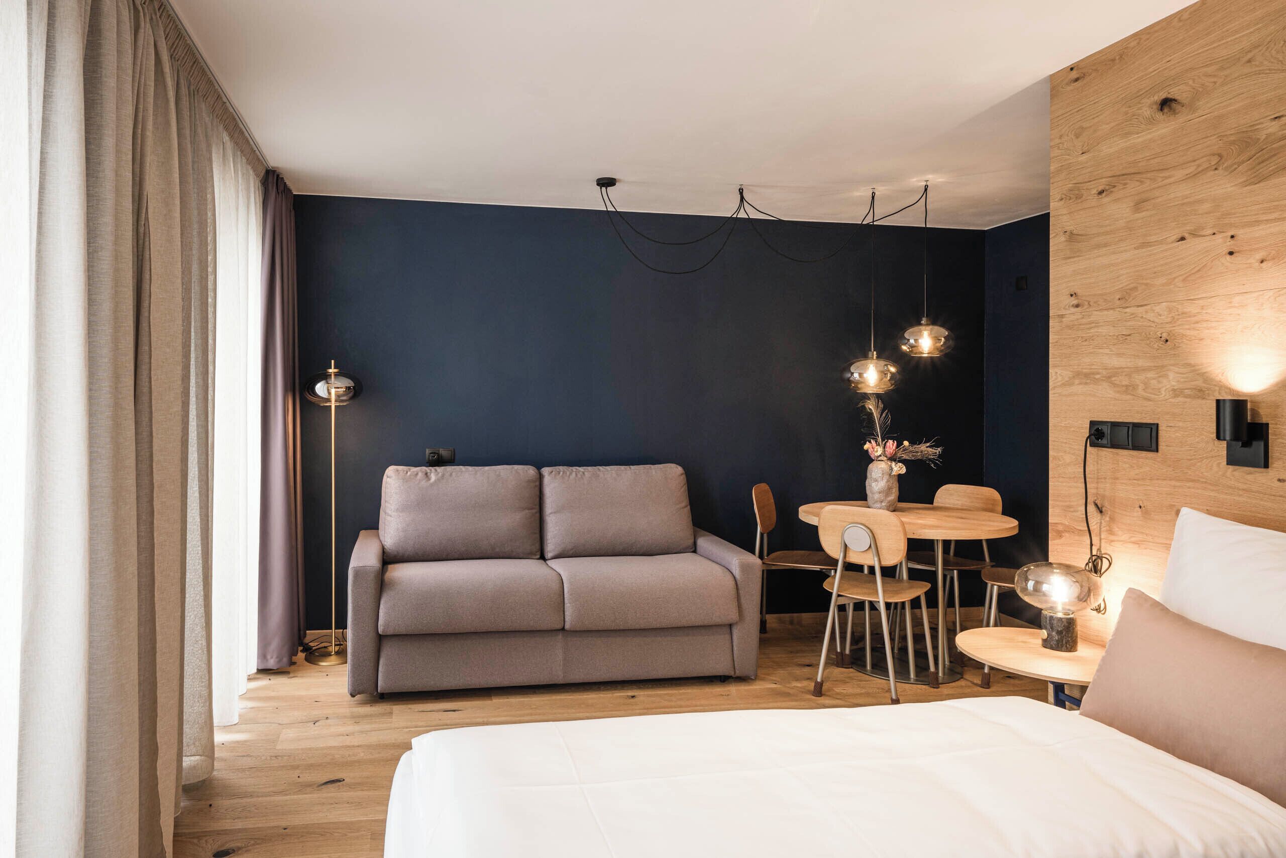 A modern hotel room with a sofa, a small dining table, and a bed.