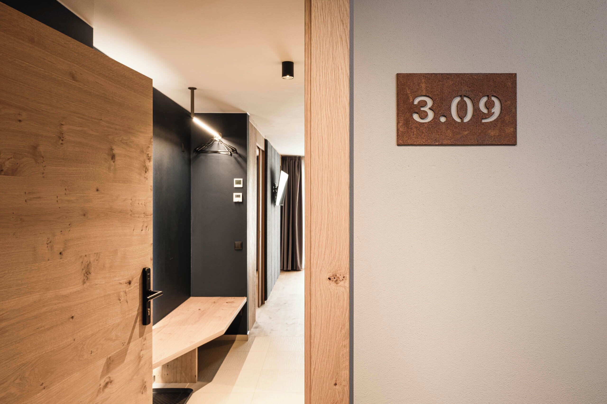 A hallway with a wooden bench, a black wall, and a sign with the number 3.09.