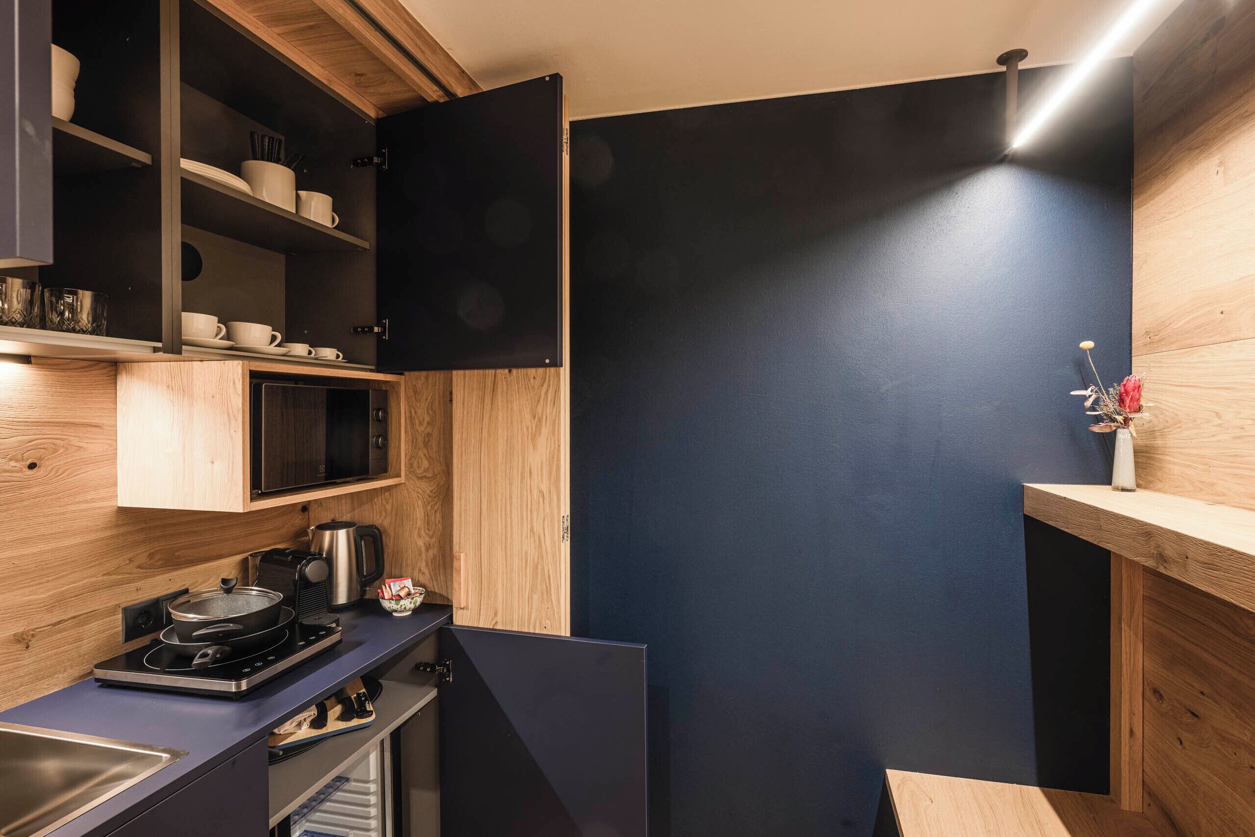 A compact kitchen with dark blue walls, wooden cabinets, and a built-in microwave.