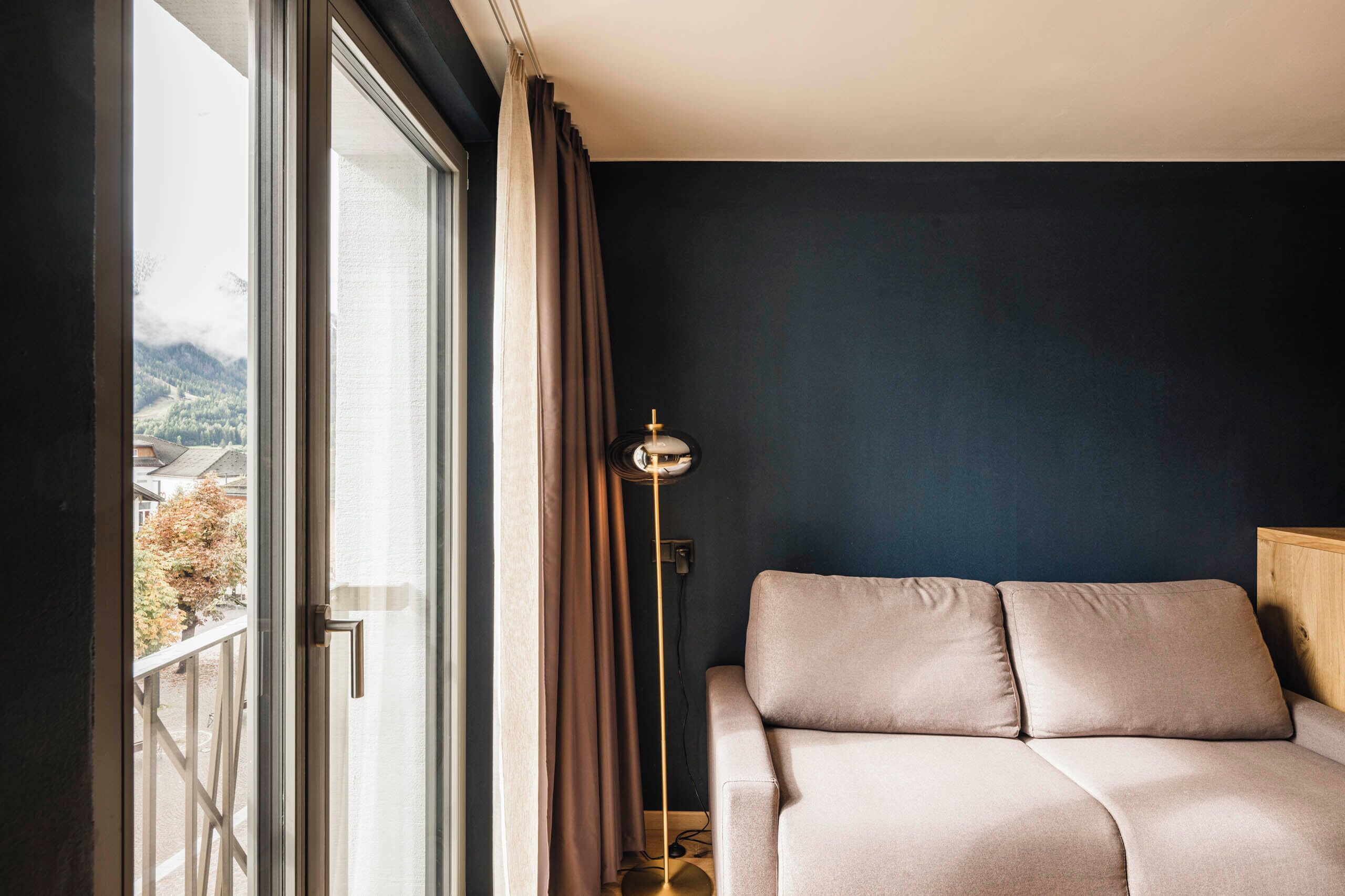 A bedroom with a bed, a floor lamp, and a view of the outdoors.