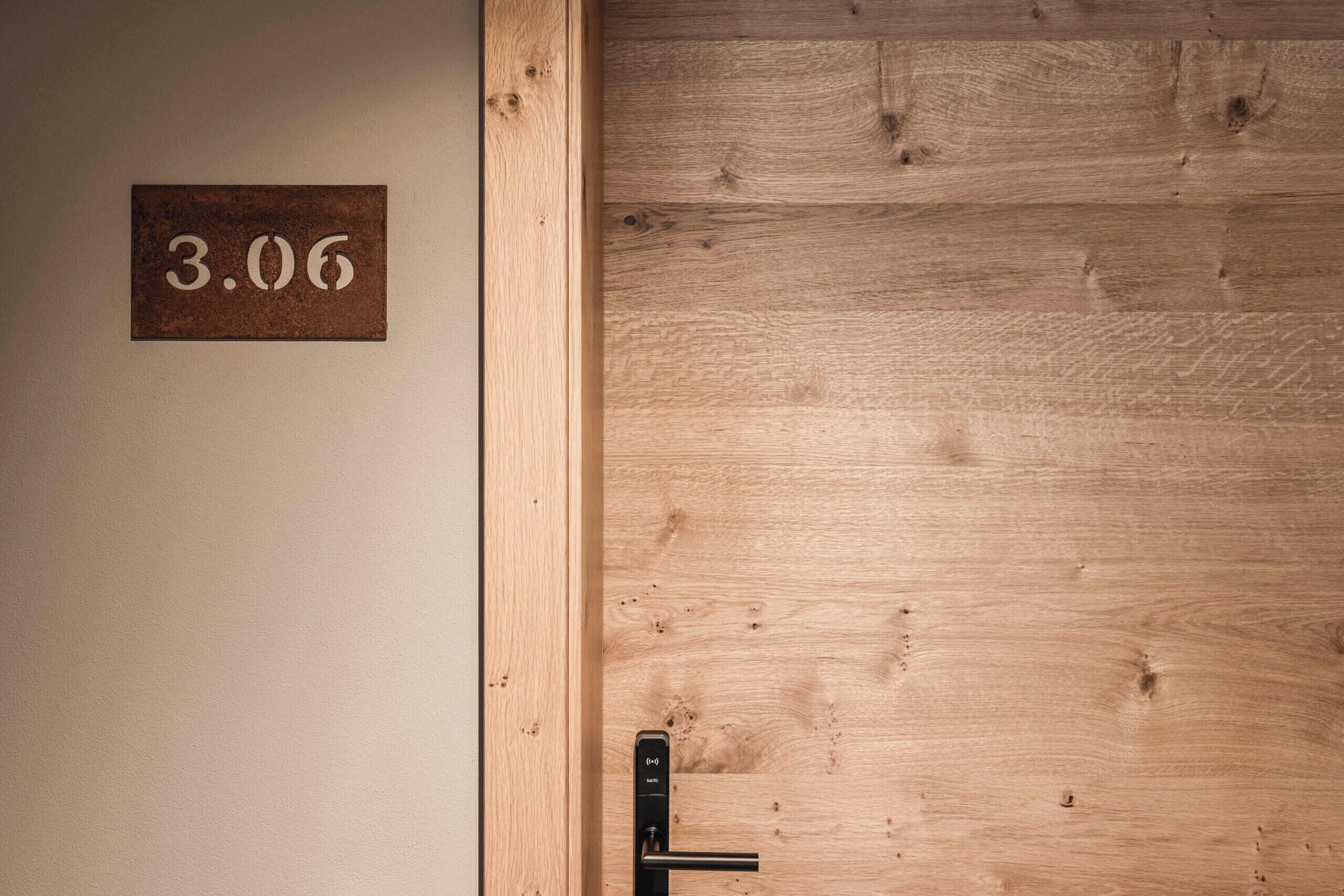 A wooden door with a metal handle and a sign above it displaying the number 3.06.