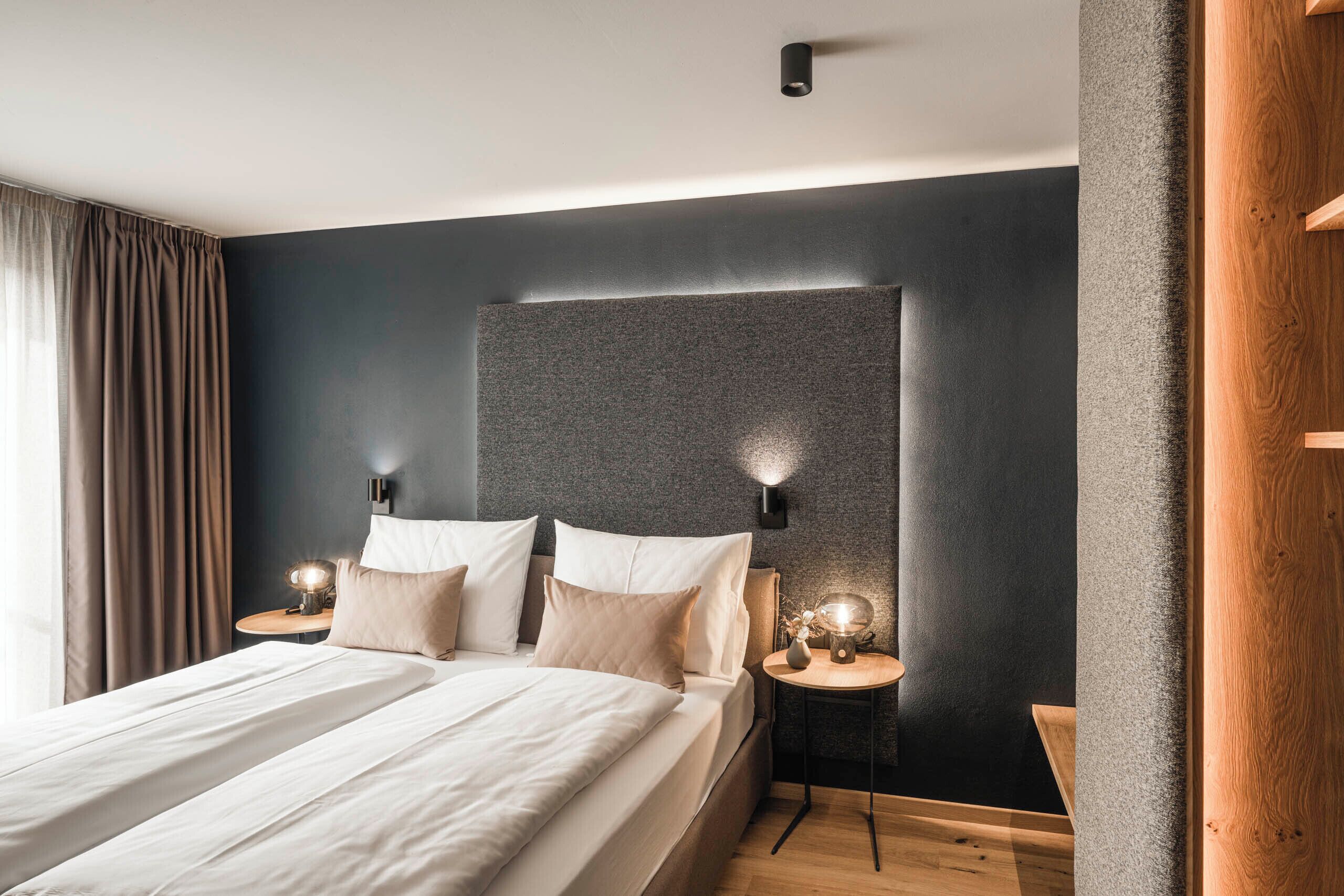 A modern bedroom with a large bed, two bedside tables with lamps, and a dark accent wall.