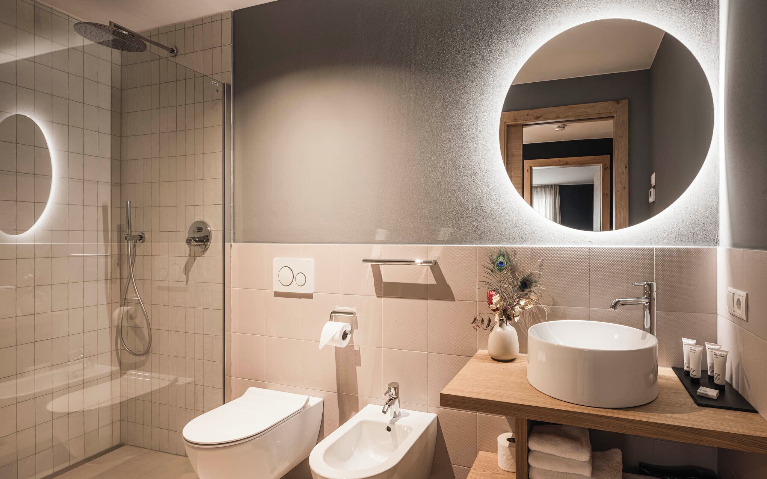 Une salle de bain moderne dotée d’une douche à parois de verre, de toilettes, d’un bidet, d’un lavabo et d’un meuble-lavabo avec des articles de toilette.
