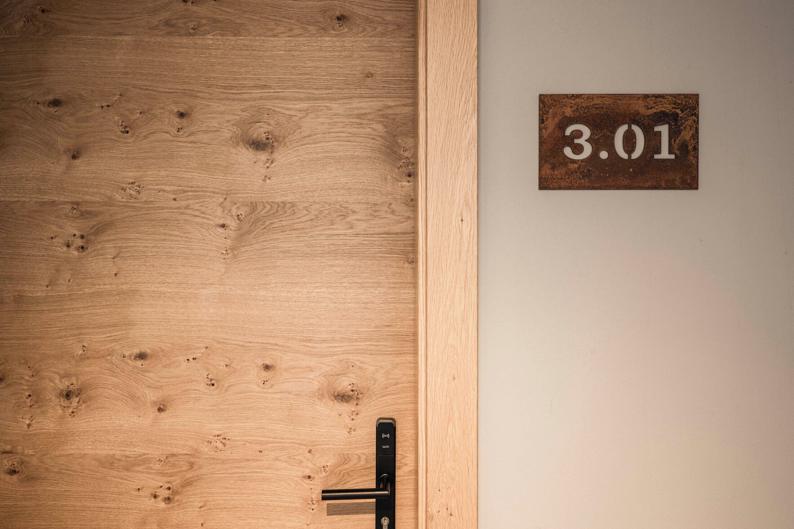 Una puerta de madera con una placa metálica que indica el número "3.01" y un picaporte moderno.