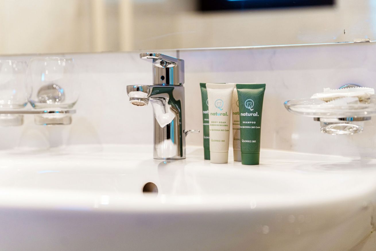 A bathroom sink with a chrome faucet, two natural body soap tubes, and a glass soap dish.
