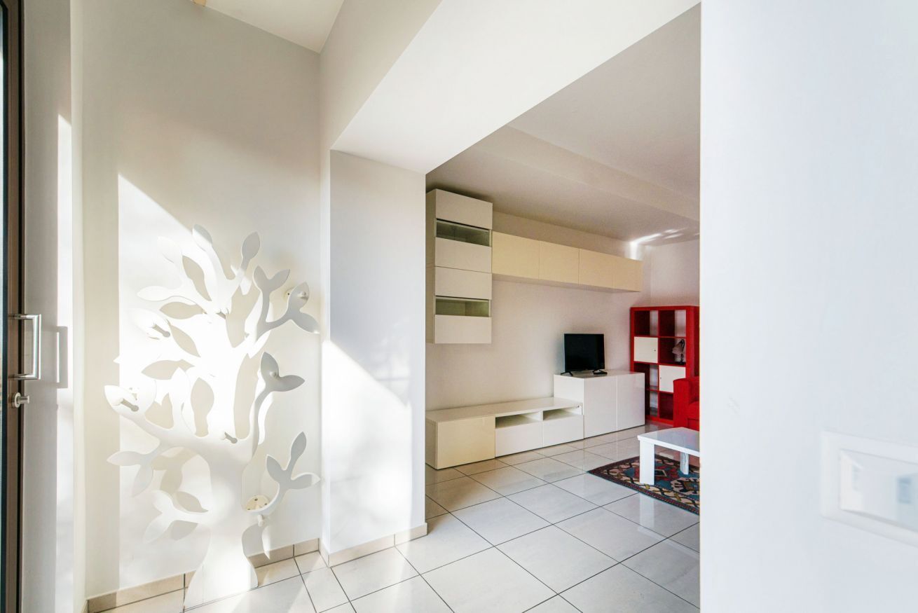 Un salon moderne avec un canapé blanc, une bibliothèque rouge et un téléviseur posé sur un meuble blanc.