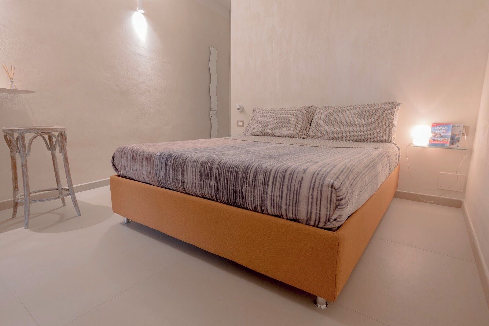Un dormitorio con cama, mesita de noche y lámpara de pared.