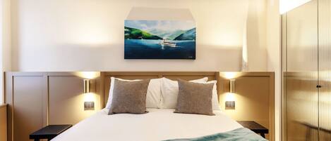 A hotel room with a bed, pillows, a painting of a lake, and a tray with breakfast items.