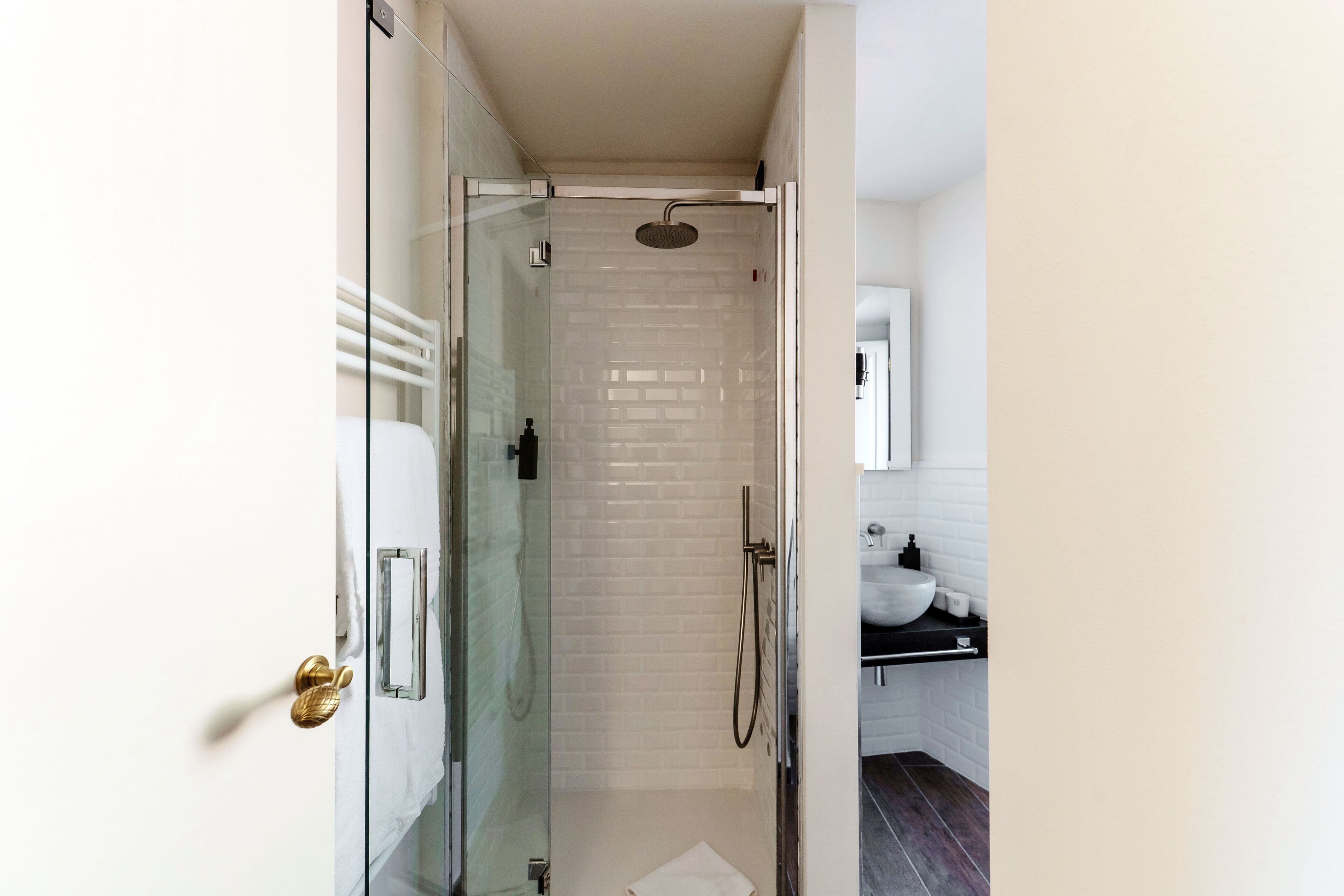 Un baño moderno con ducha de vidrio, azulejos blancos tipo metro, lavamanos blanco y encimera negra.