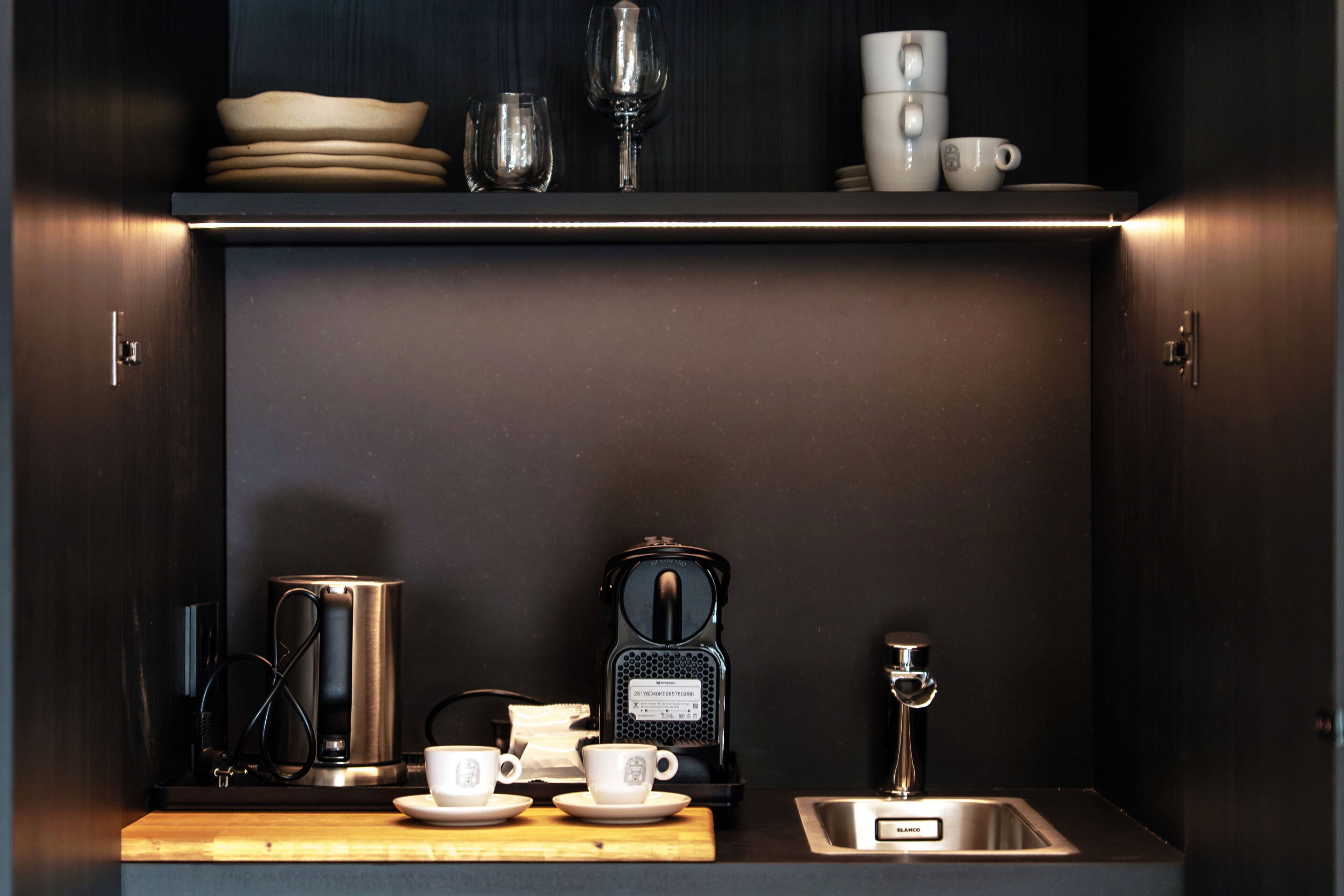 Une petite cuisine équipée d’une machine à café, de tasses et d’un évier.
