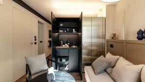 A compact living space with a sofa, a small table, and a kitchenette area. - Home Holidays (Argegno)