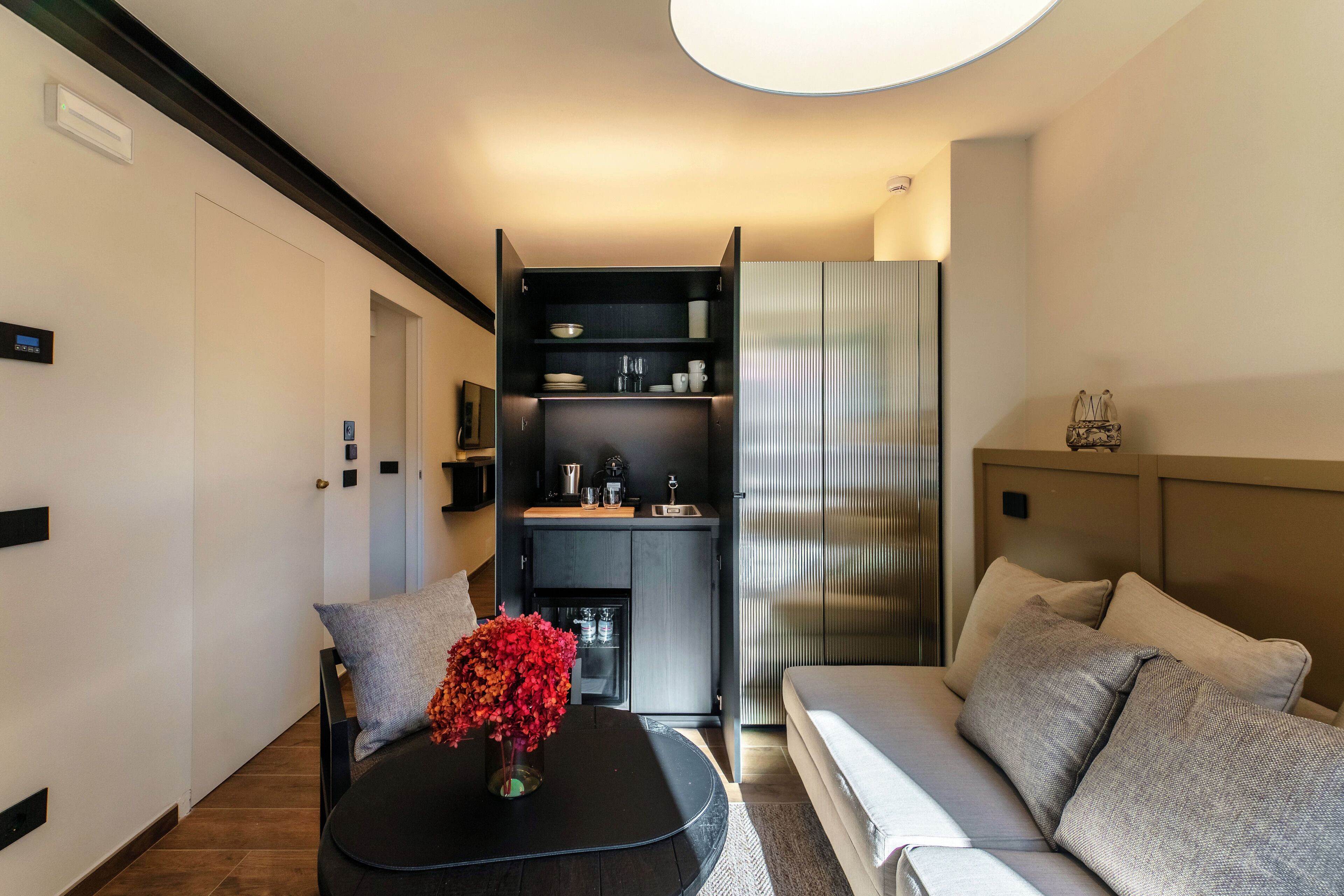 Una sala de estar moderna con un sofá, una mesita de centro y una zona de cocina con un refrigerador y alacenas.