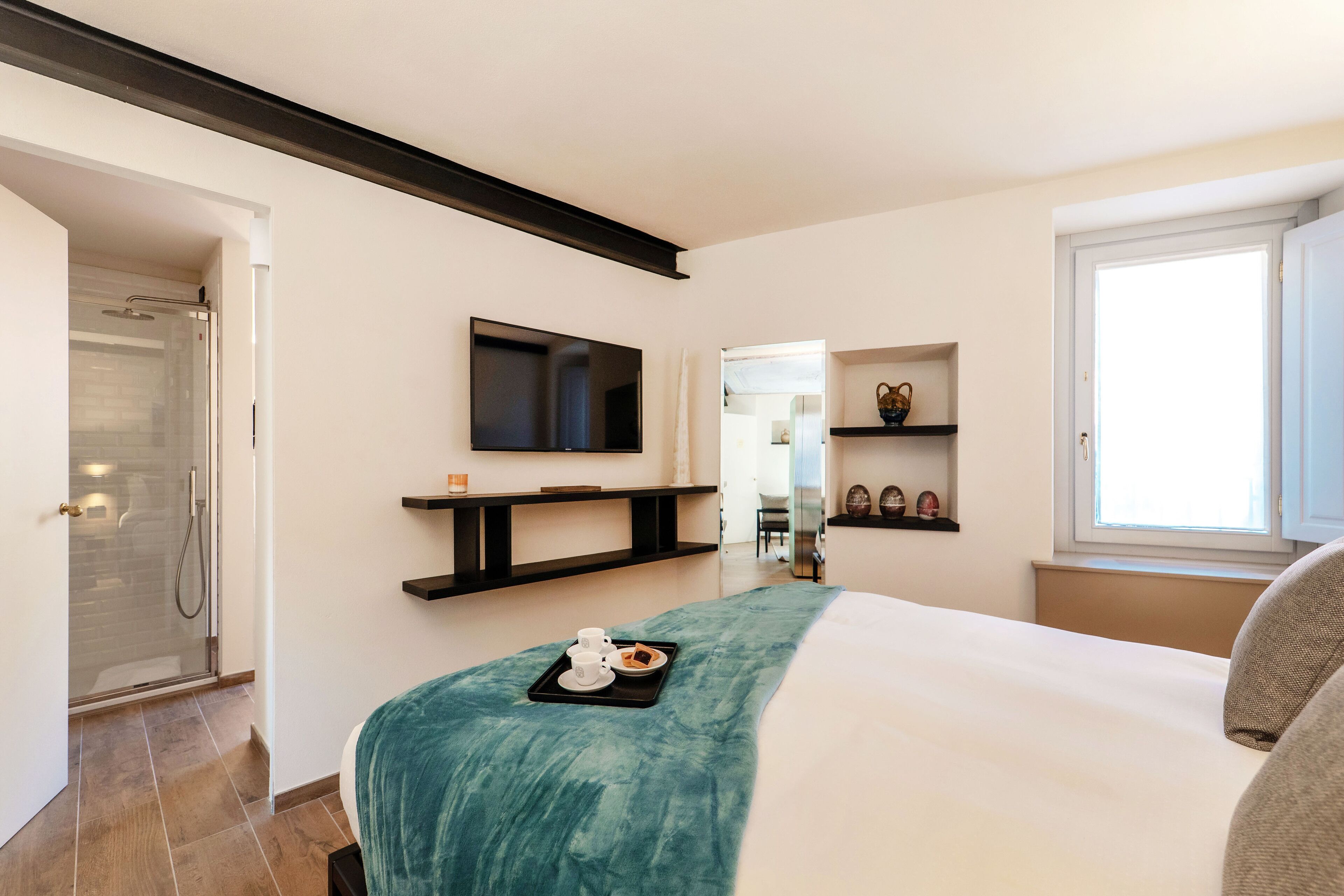 Een moderne hotelkamer met een groot bed, een aan de muur bevestigde televisie, een douchegedeelte en een ontbijttray op het bed.