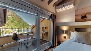 A hotel room with a large window, a bed, a bedside table, a lamp, and a view of a mountain. - Home Holidays (Argegno)
